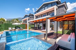 A modern house with a swimming pool, outdoor seating, and a covered patio area.