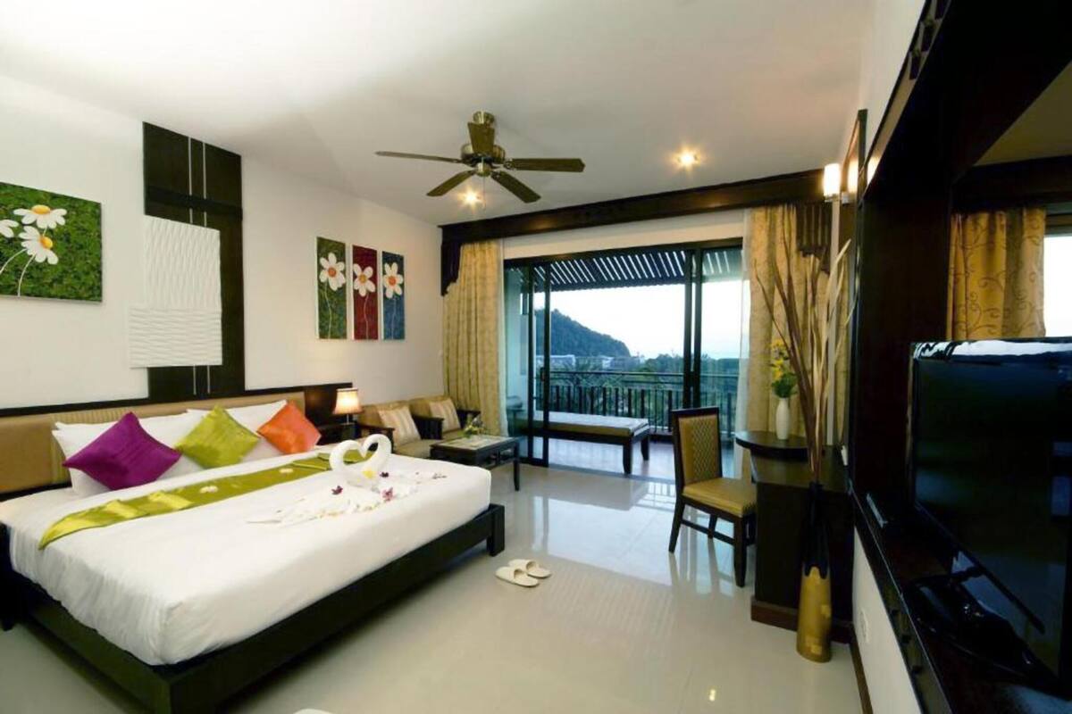 A hotel room with a bed, a TV, a balcony with a view, and a ceiling fan.