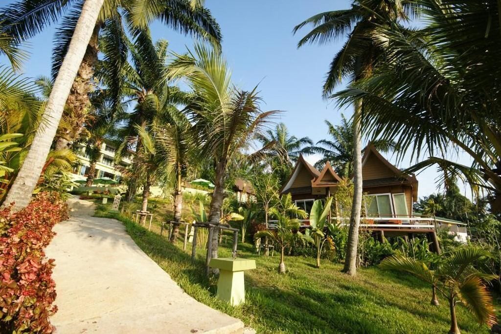 A pathway lined with palm trees leading to a resort with wooden structures and a clear sky.
