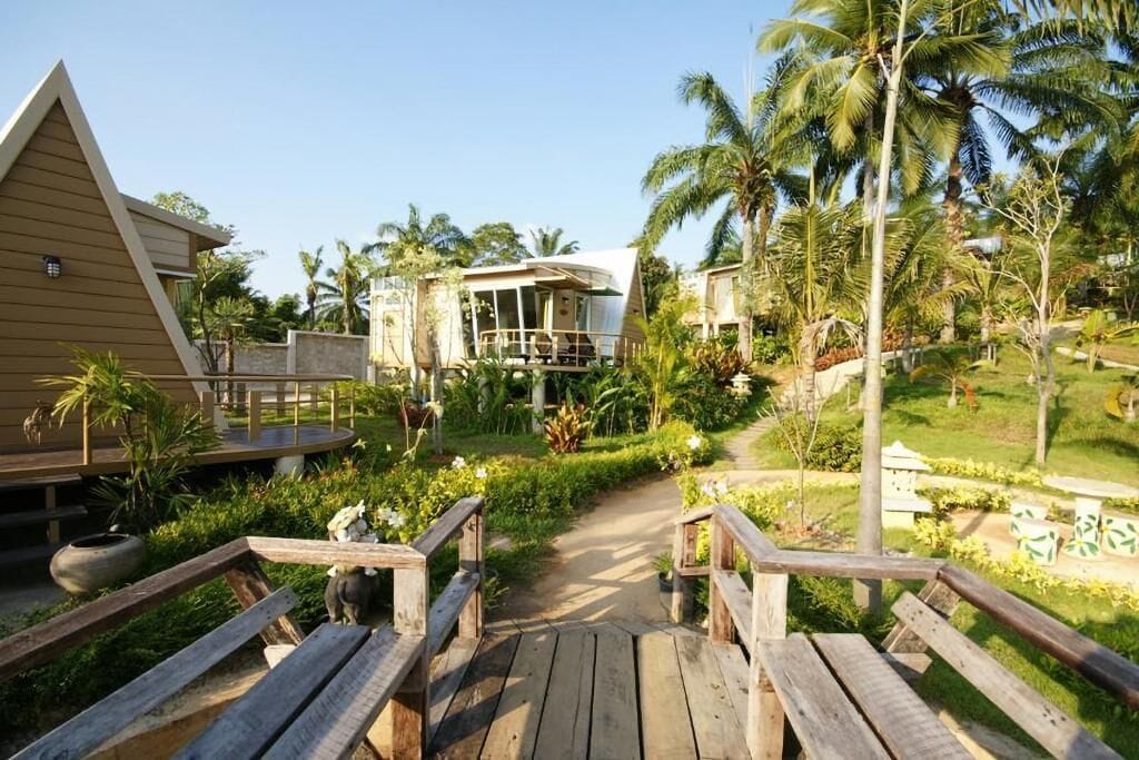 A resort with wooden walkways, palm trees, and a clear sky.