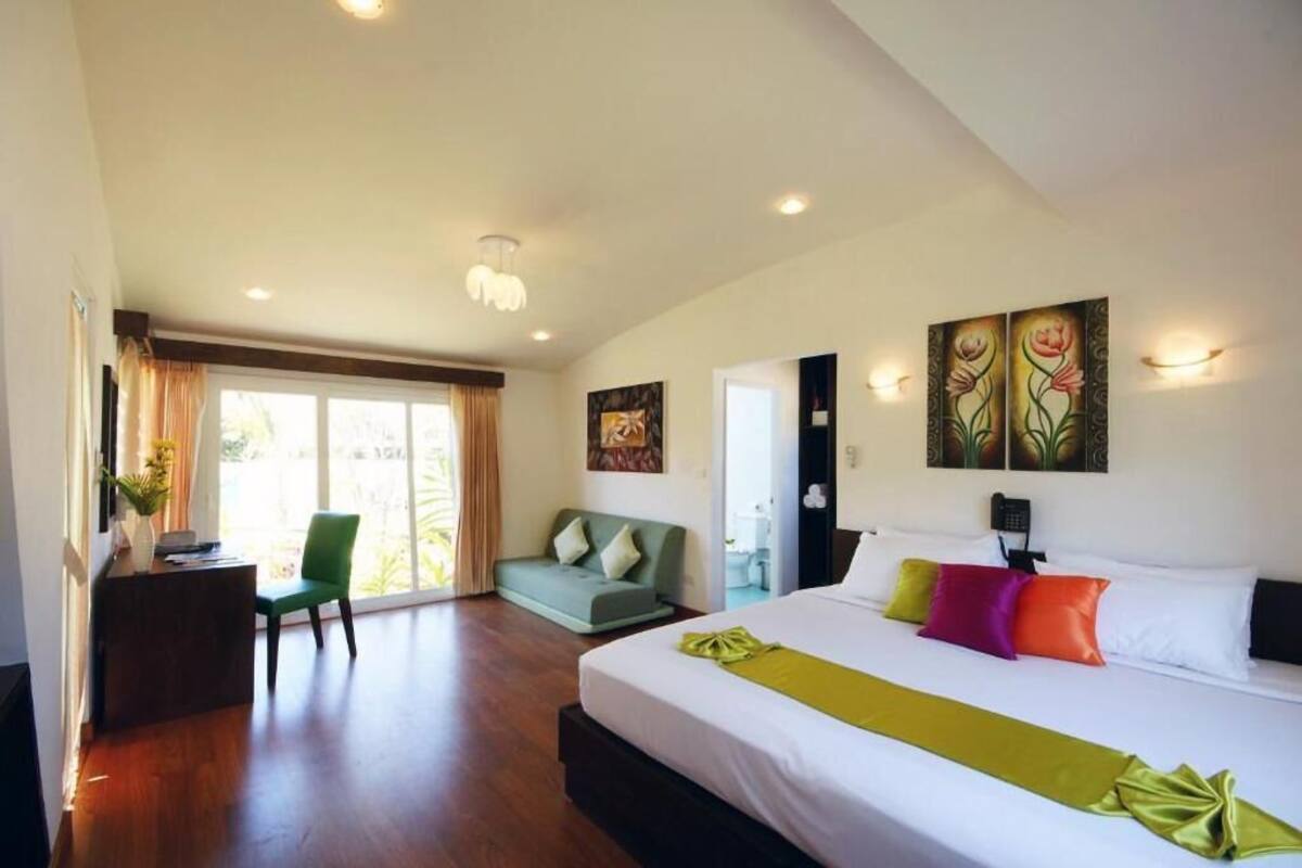 A hotel room with a large bed, a desk, a green sofa, and artwork on the walls.