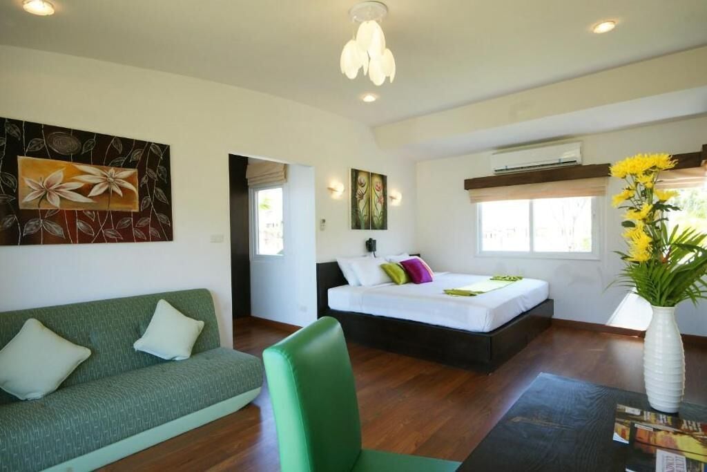 Un dormitorio moderno con un sofá verde, una cama con almohadas coloridas, un jarrón con flores amarillas y obras de arte en las paredes.