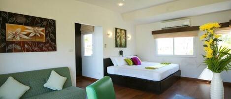 Un dormitorio moderno con un sofá verde, una cama con almohadas coloridas, un jarrón con flores amarillas y obras de arte en las paredes.