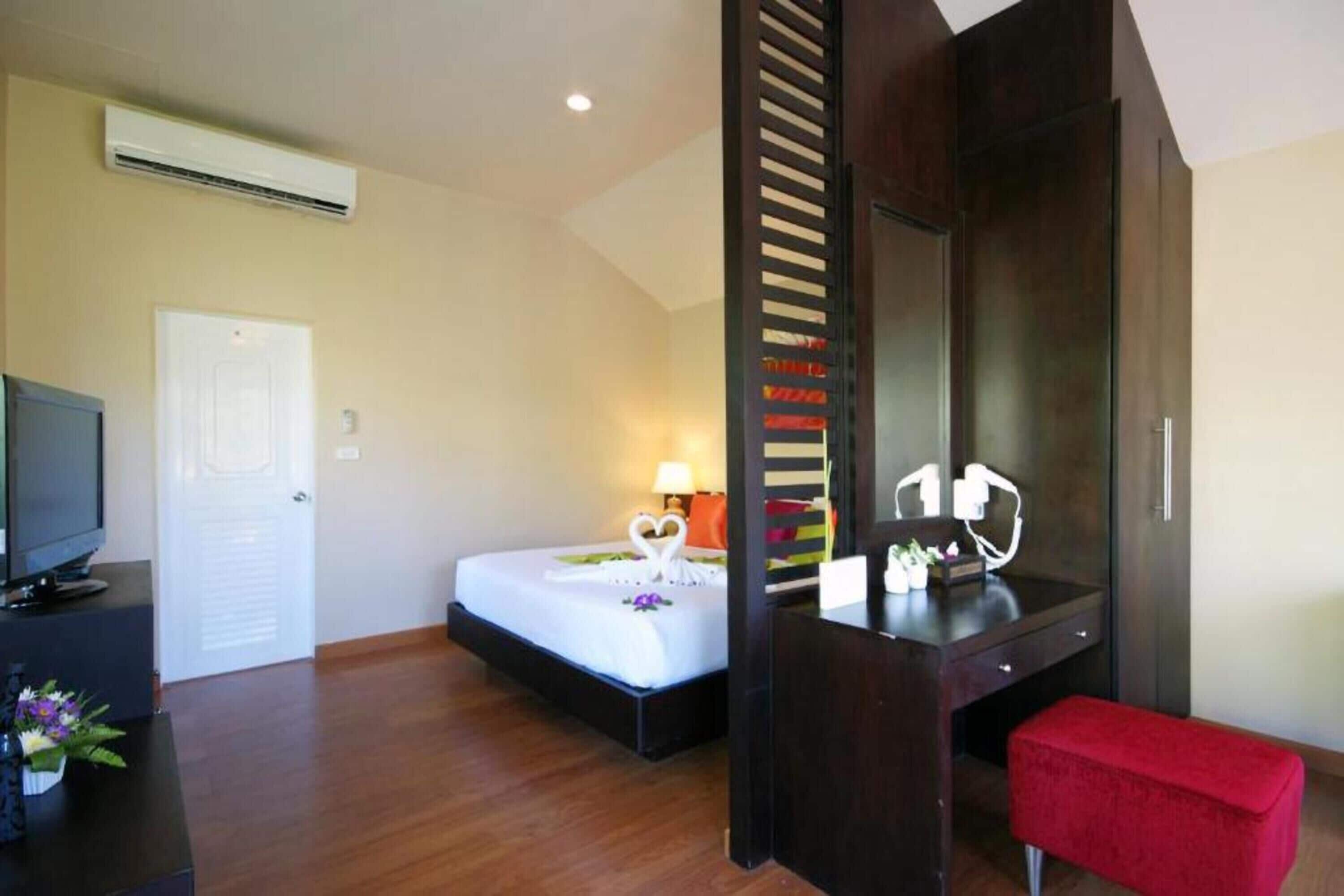 Une chambre d’hôtel avec un lit, un bureau, une télévision et un banc rouge.