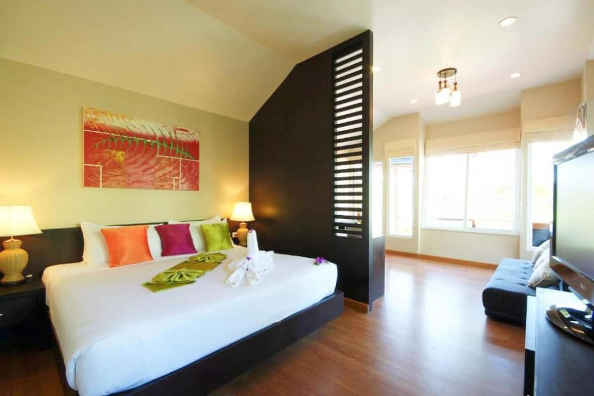 A hotel room with a large bed, a flat-screen TV, a desk, and a window with natural light.
