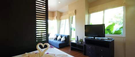 A hotel room with a bed, a TV, a sofa, and a window with a view of greenery.