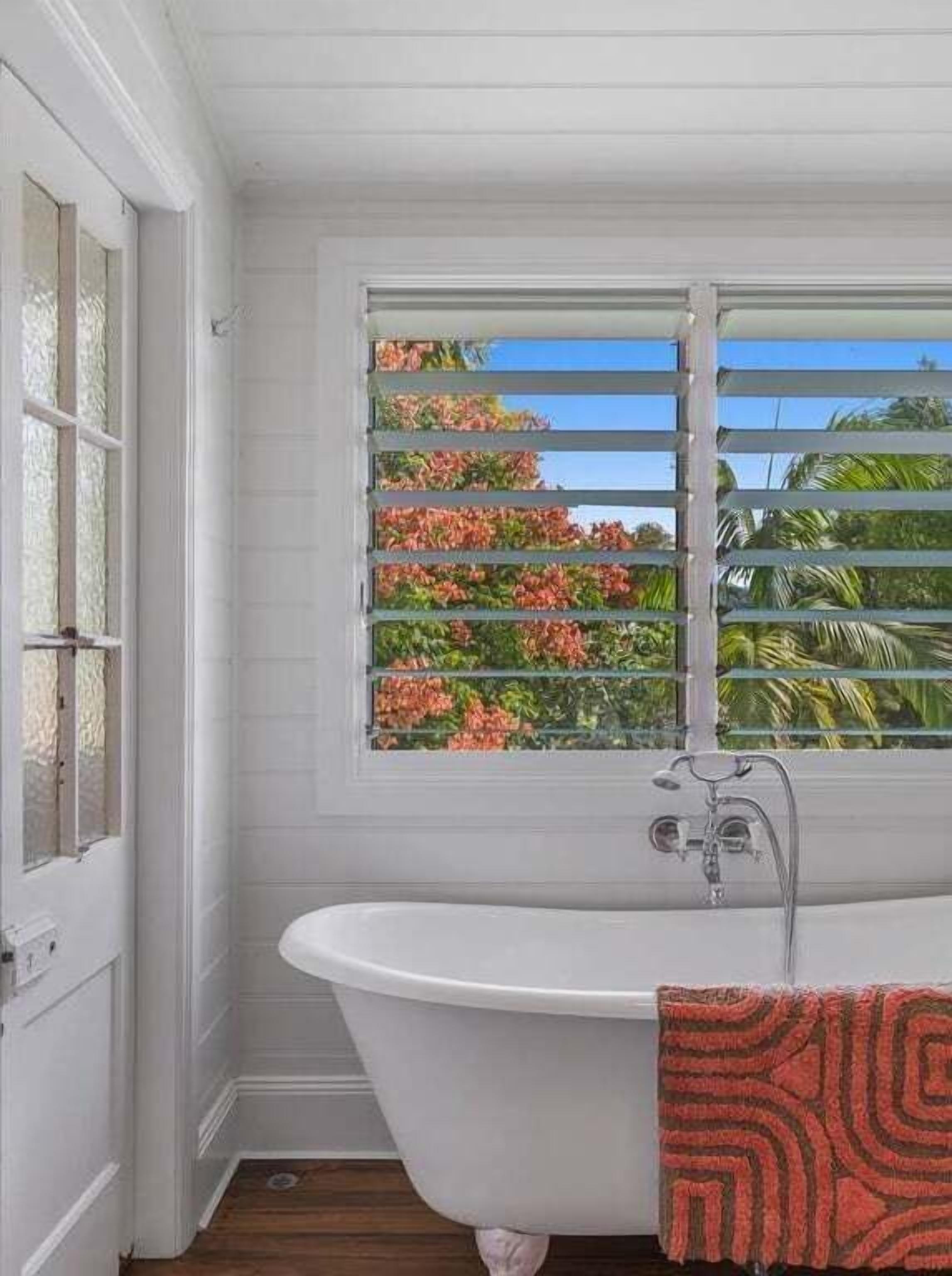 A bathroom with a white bathtub, a window with a view of greenery, and a door with a window.