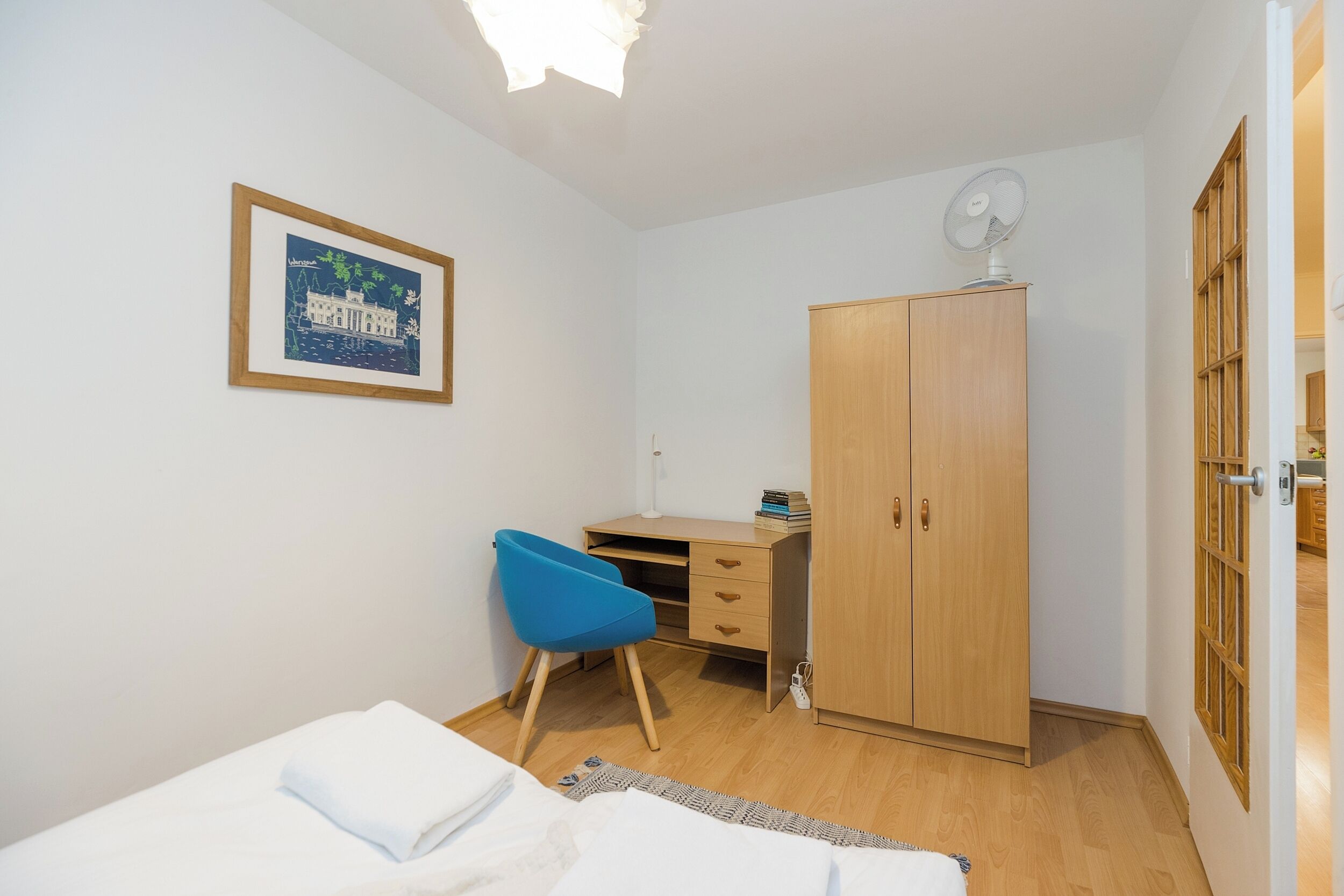 Un dormitorio con cama, escritorio, silla, armario y un cuadro en la pared.
