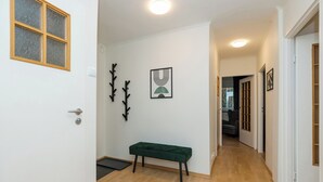 A hallway with a wooden floor, a green bench, a coat rack, and a framed picture on the wall. - ShortStayPoland Piekałkiewicza B112 (Warsaw)