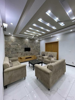 A modern living room with a stone accent wall, a flat-screen TV, and a ceiling fan. - Pyramid Guest House (Islamabad)