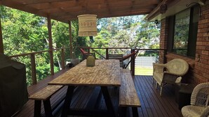 Una terraza de madera con una mesa de picnic y sillas de mimbre, con vistas a un paisaje verde exuberante.