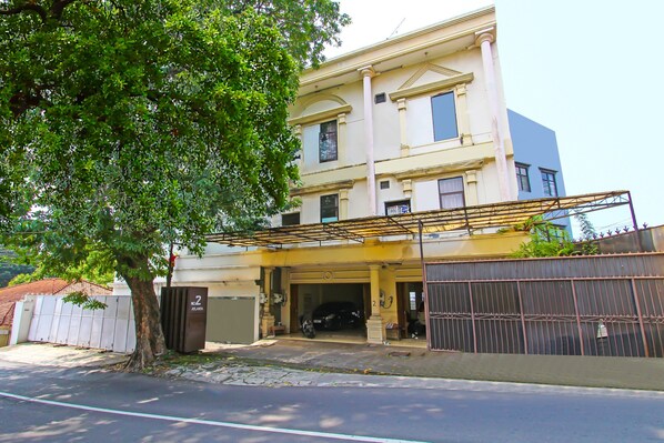 A two-story building with a garage entrance, a tree in front, and a gated driveway. - Hotel O Atlanta Guesthouse (Semarang)