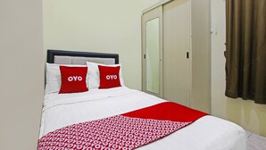 A bed with white bedding and red pillows, a red and white patterned throw, and a wardrobe with a mirror. - Hotel O Atlanta Guesthouse (Semarang)