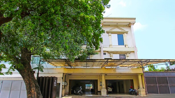 A building with a covered entrance, a tree in front, and two parked motorcycles. - Hotel O Atlanta Guesthouse (Semarang)