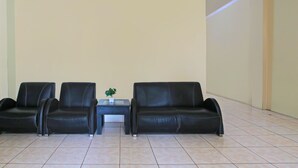 A waiting area with two black leather sofas, a small table with a plant, and a tiled floor. - Hotel O Atlanta Guesthouse (Semarang)