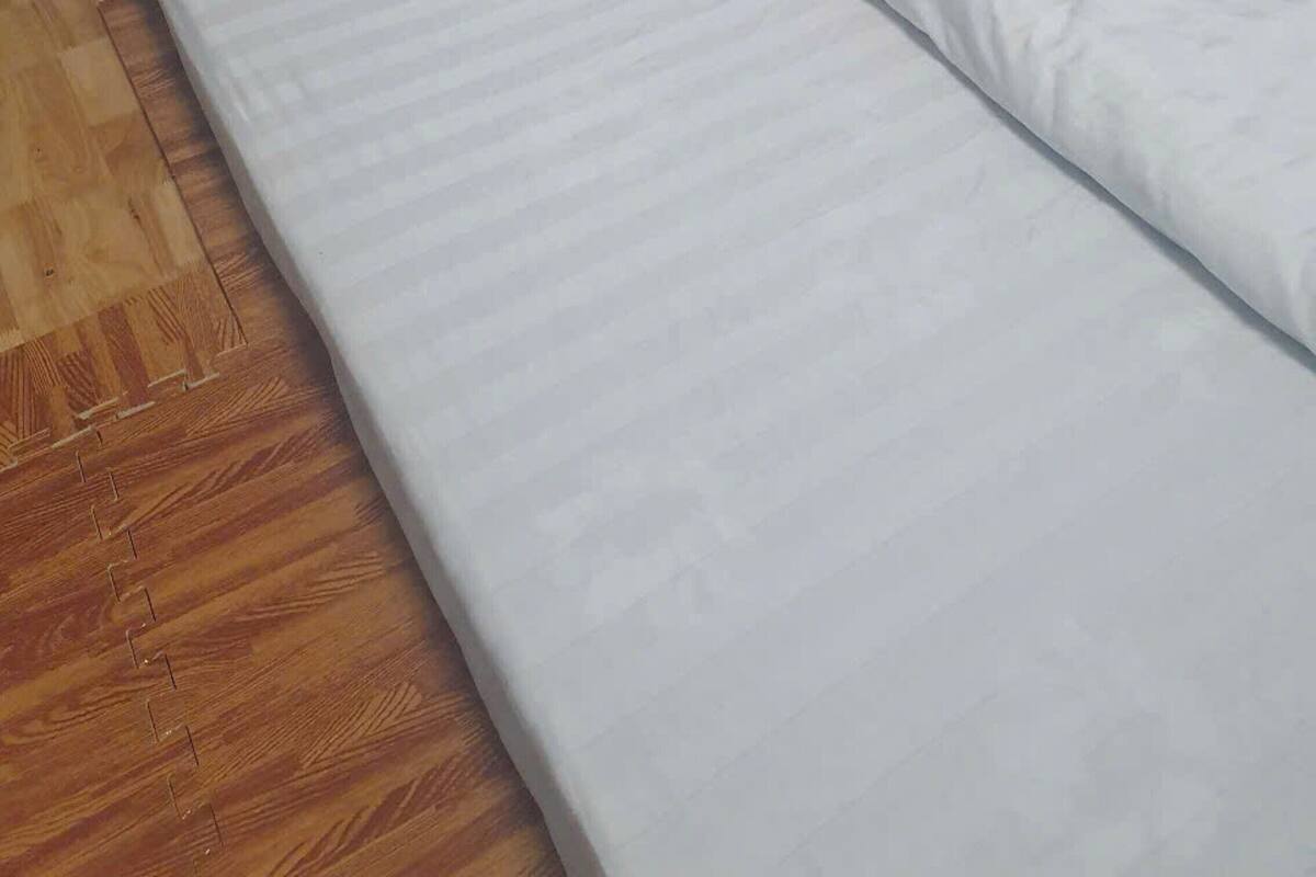 A bed with white bedding in a room with wooden flooring and a wooden headboard.