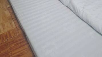 A bed with white bedding in a room with wooden flooring and a wooden headboard.