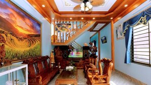 A spacious living room with a wooden staircase, a large painting, and a television. - Ha Chau Homestay (Mu Cang Chai)