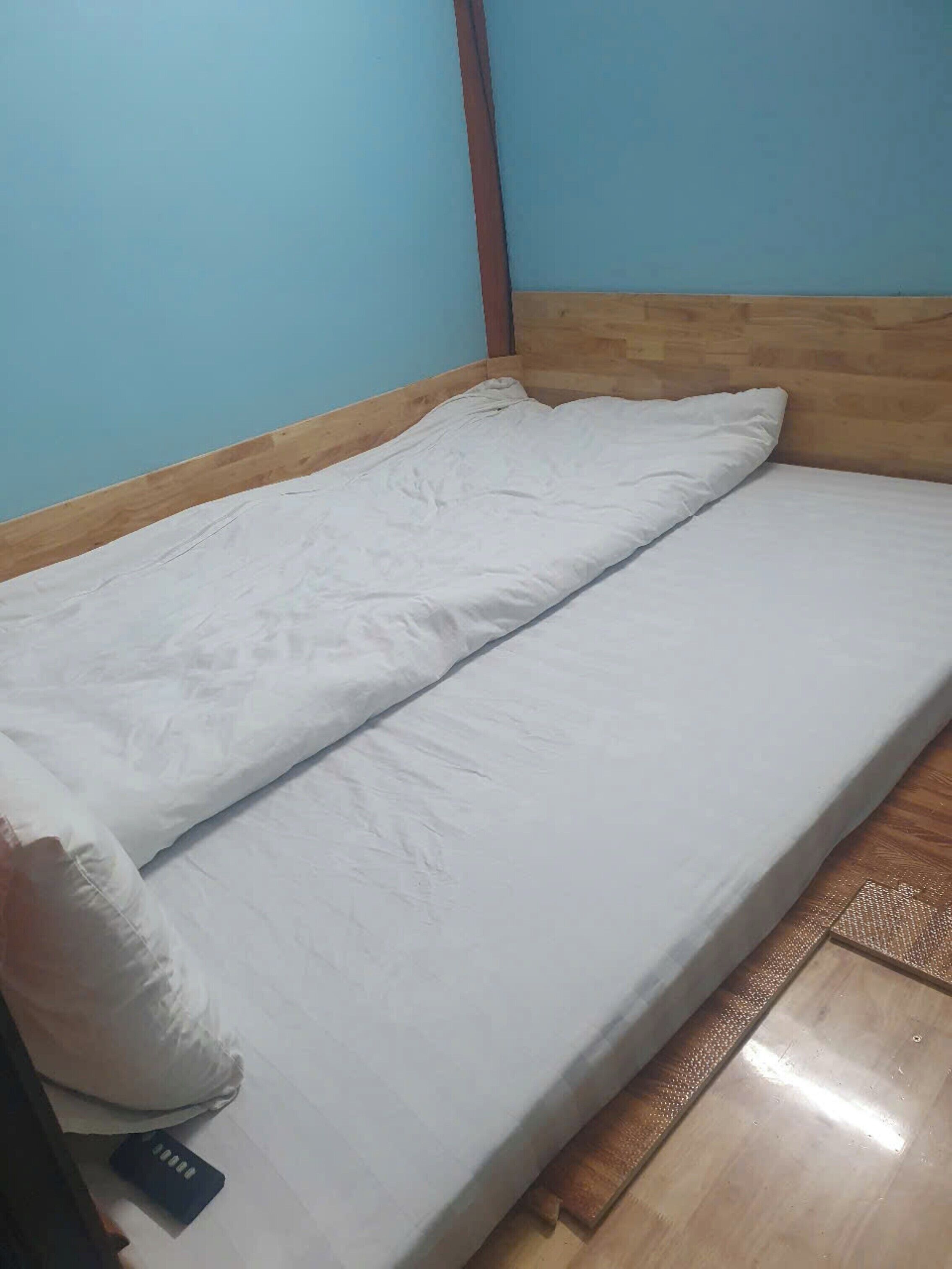 A single bed with white bedding in a room with blue walls and wooden headboard.