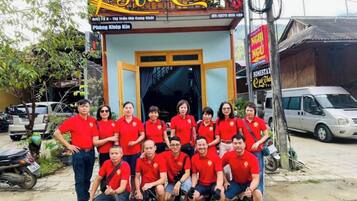 A group of people in red shirts posing in front of a building with a sign reading "Hà Châu".