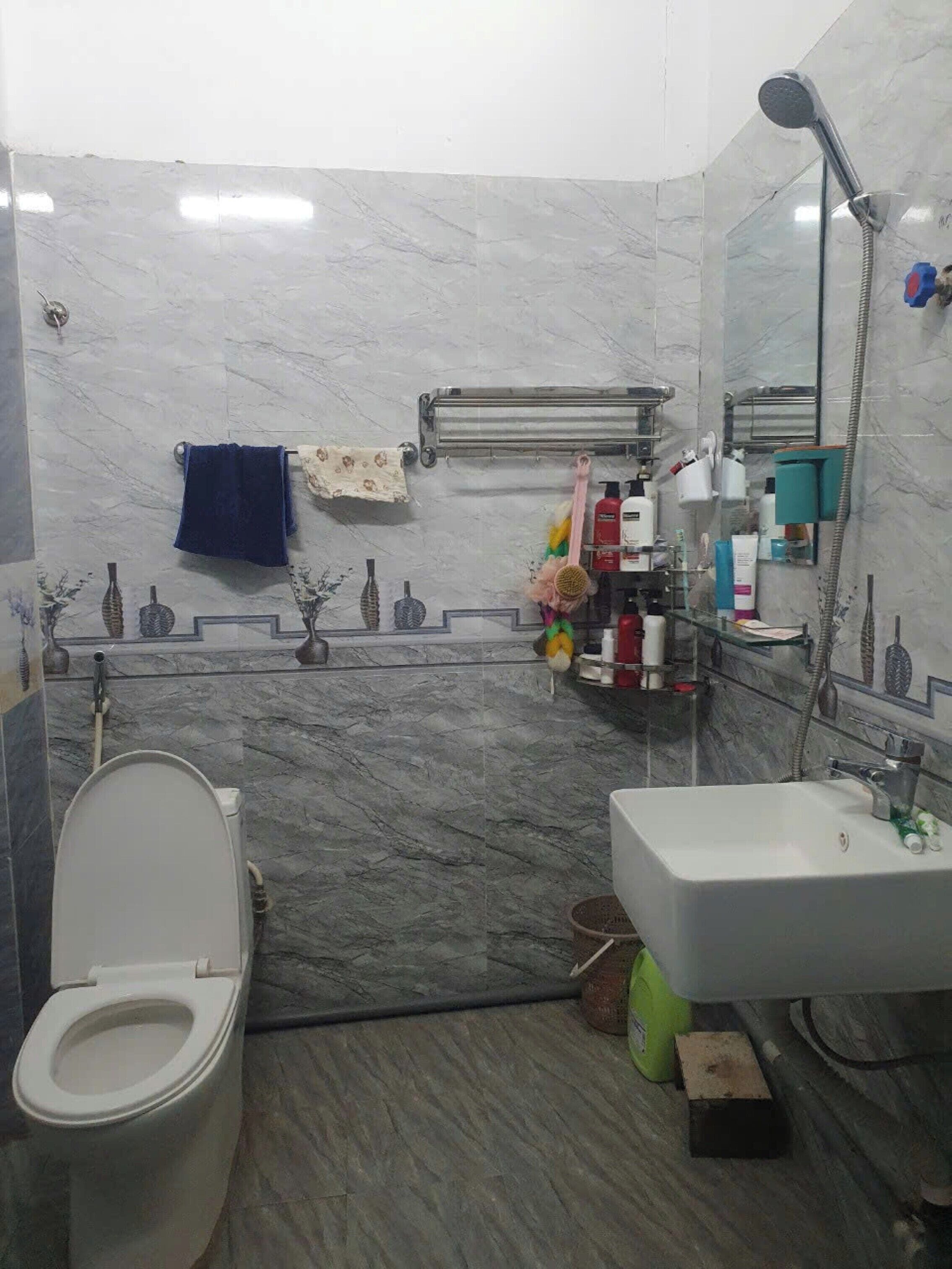 Baño con inodoro, lavamanos y ducha. Hay artículos de aseo y un perchero para toallas.