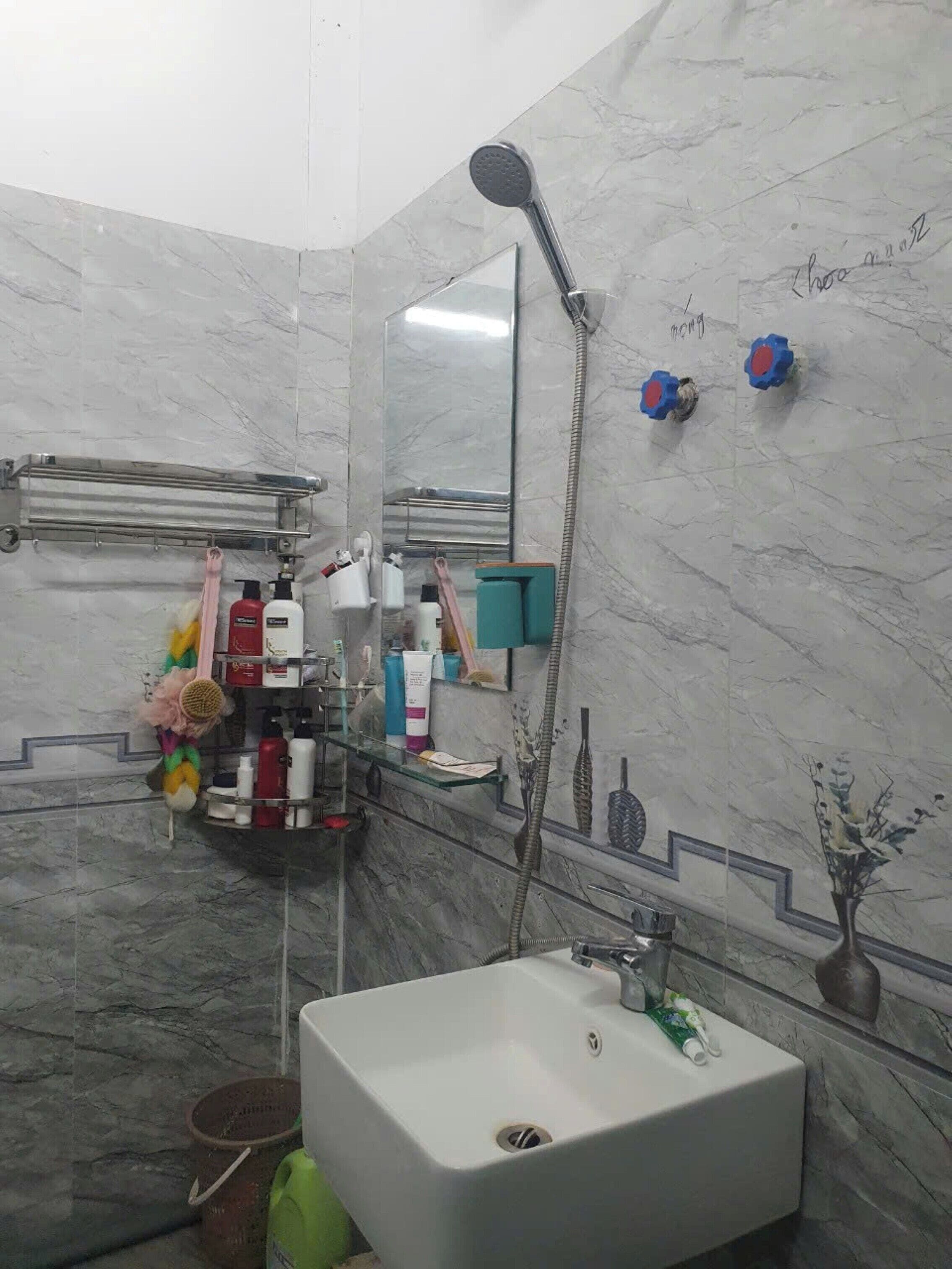 A bathroom with a large mirror, a shower, a sink, and various toiletries on shelves.