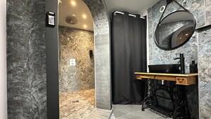 Een moderne badkamer met een douchewand van steen, een zwart douchegordijn, een houten wastafelmeubel met een zwart wastafel en een ronde spiegel.