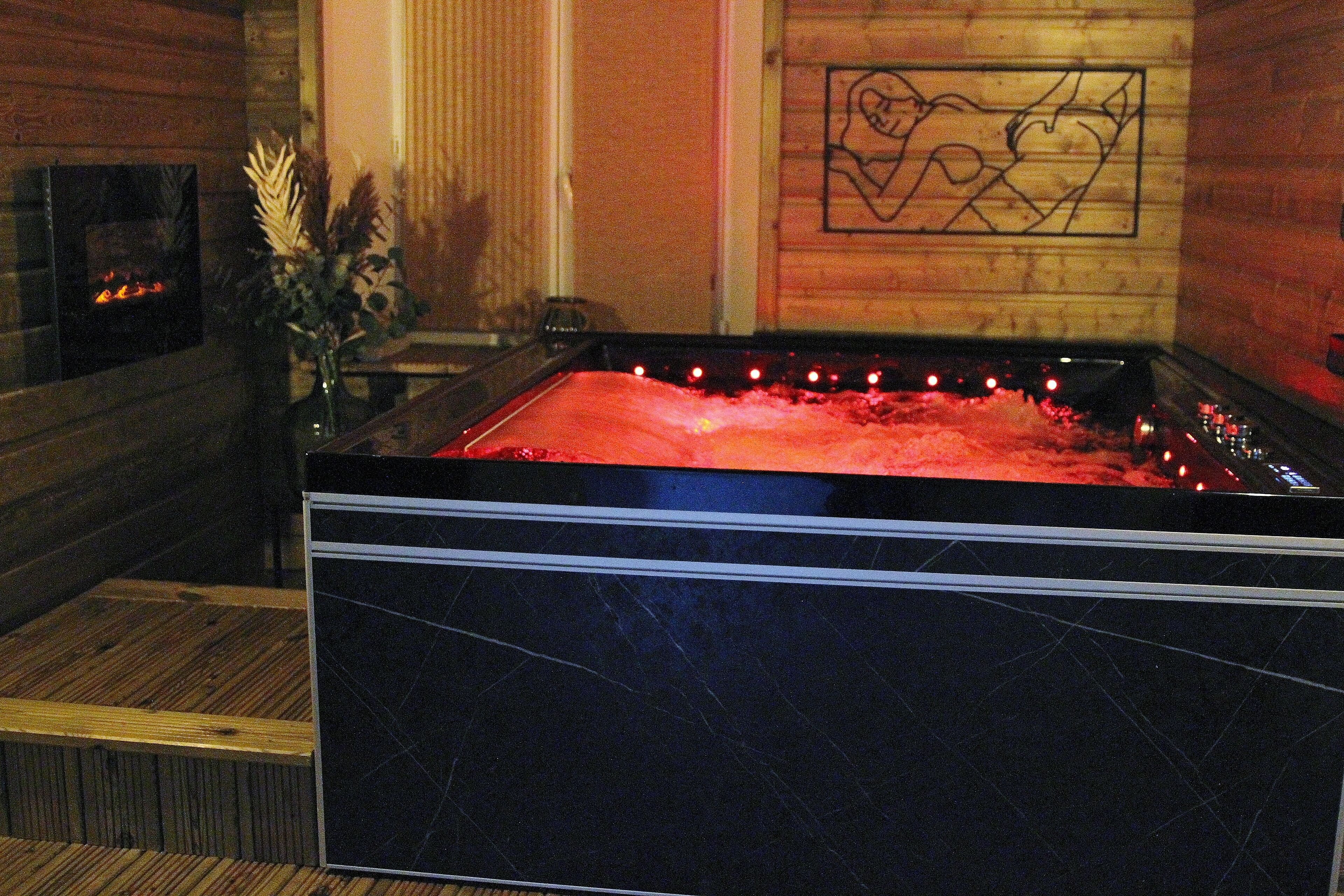 Uma área de spa com uma banheira de mármore preto, uma parede de madeira com um mural e uma lareira.