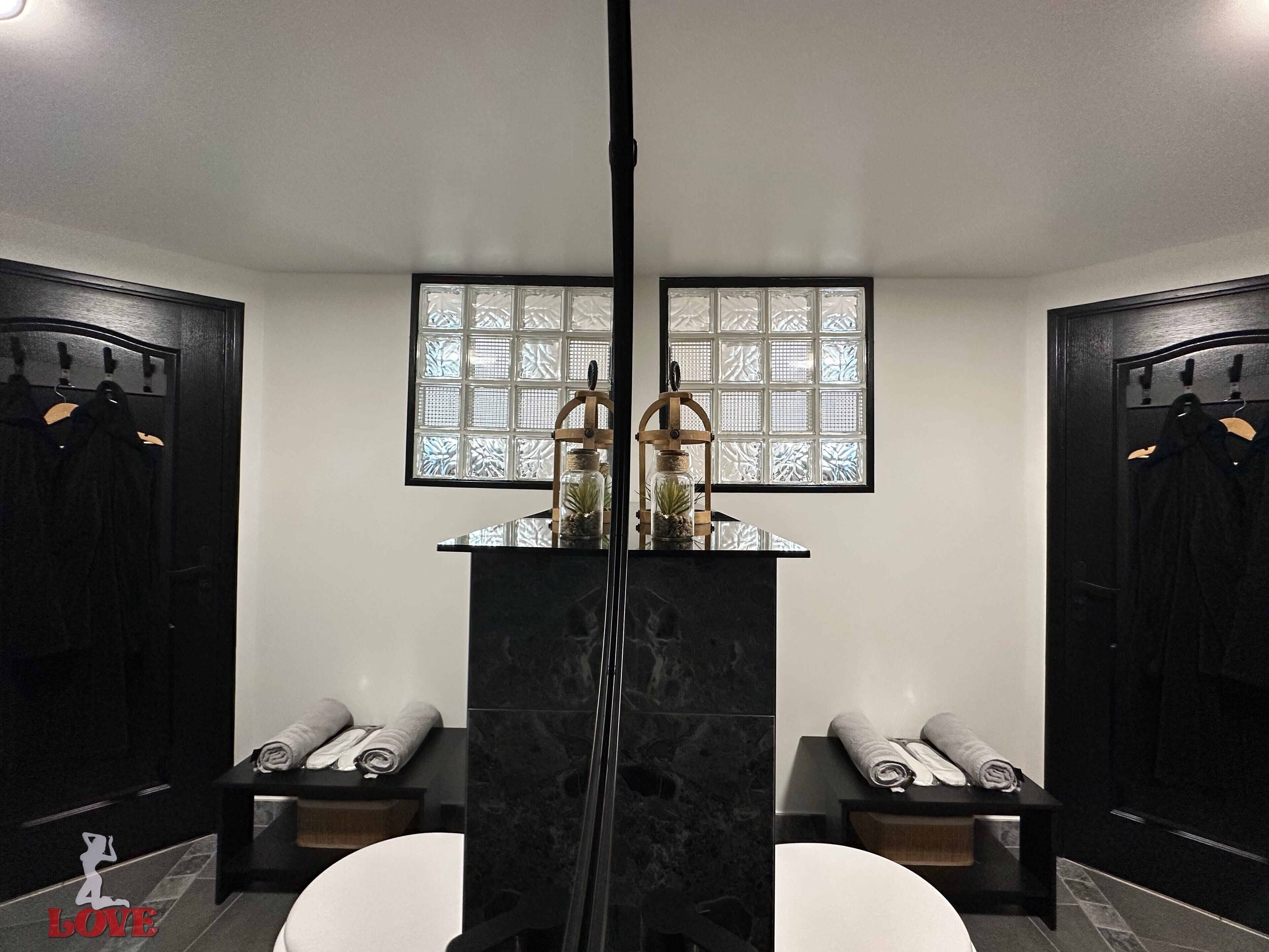 Un baño moderno con un lavamanos central de mármol, dos bancos cubiertos con toallas y una ventana con paneles de vidrio esmerilado.