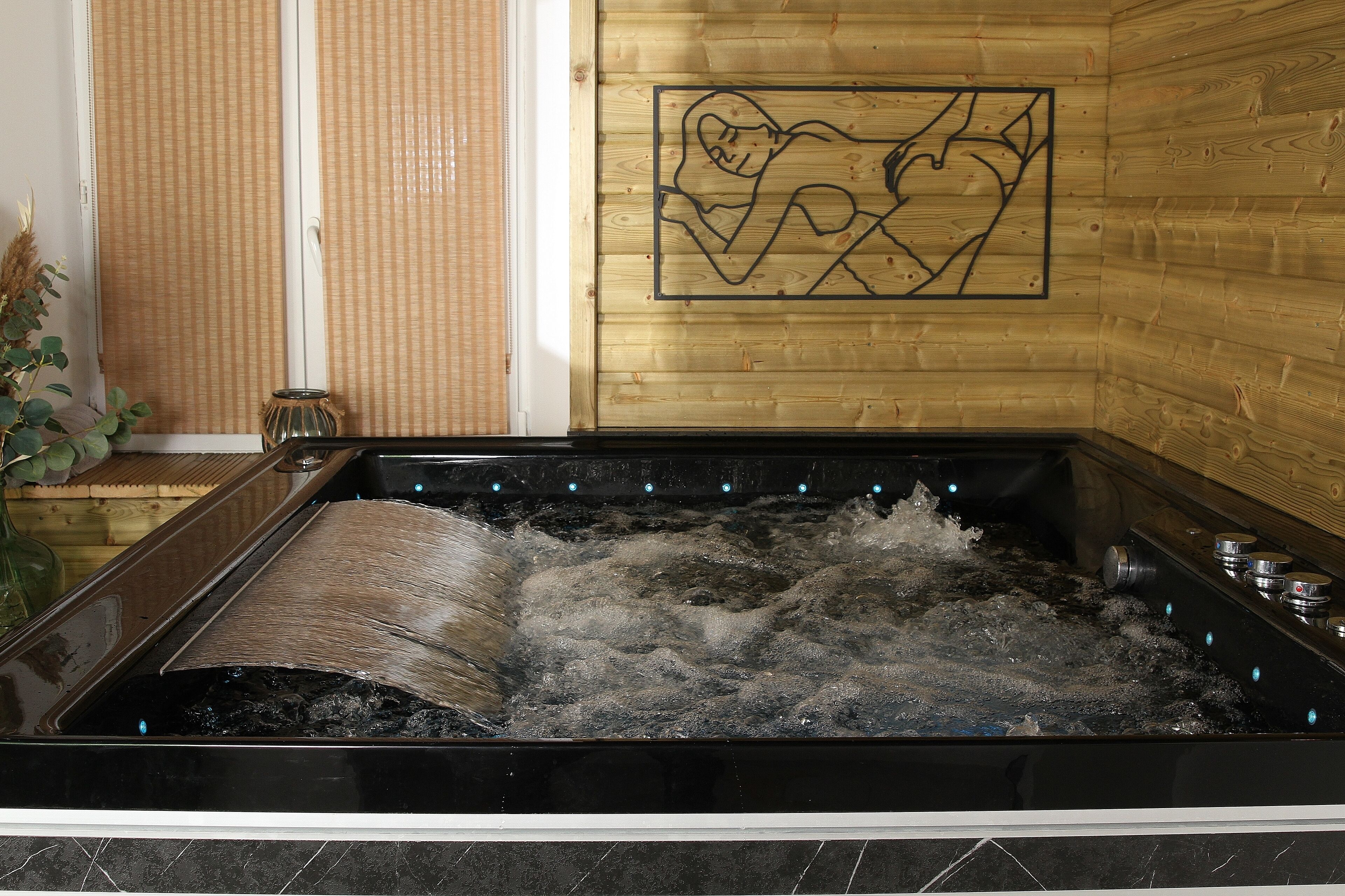 Ein Whirlpool mit Wasserstrahlen, eine Holzverkleidung mit Herzmotiv und ein Bambusrollvorhang.