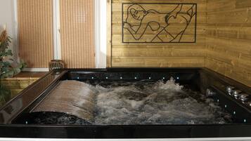 Ein Whirlpool mit Wasserstrahlen, eine Holzverkleidung mit Herzmotiv und ein Bambusrollvorhang.