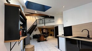 Een ruime woonkamer met keuken, een trap naar een hoger gelegen verdieping, en een barhoek.