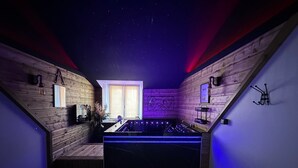 Een kamer met een sterrenhemelplafond, houten wanden, een groot raam en een zwarte pooltafel.