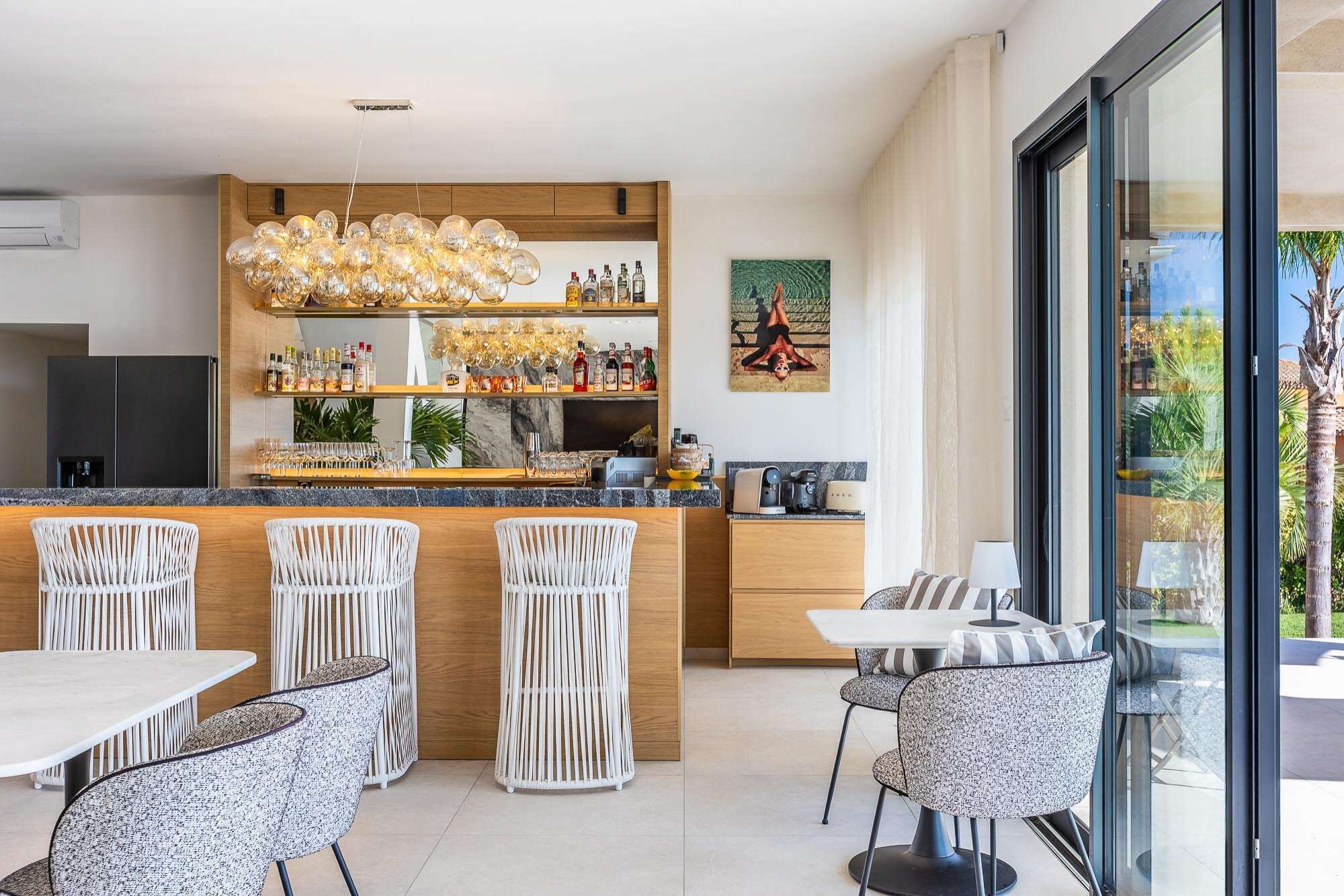 Una cocina moderna con barra, que incluye una lámpara de techo original, taburetes de bar y un comedor con vistas al exterior.