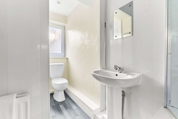A modern bathroom with a white toilet, a pedestal sink, and a mirror.