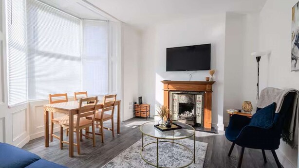 A living room with a fireplace, a TV mounted on the wall, a dining table with chairs, and a blue sofa. - Fabulous 6 bedroomed, all en-suite accommodation (Hartlepool)
