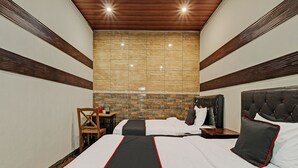 A hotel room with a large bed, a wooden headboard, a stone accent wall, and a small table with a chair. - Capital O 92276 Hotel Pesona Gunung (Getasan)