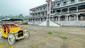 A yellow vintage car parked in front of a multi-story building with balconies and a stone wall. - Capital O 92276 Hotel Pesona Gunung (Getasan)