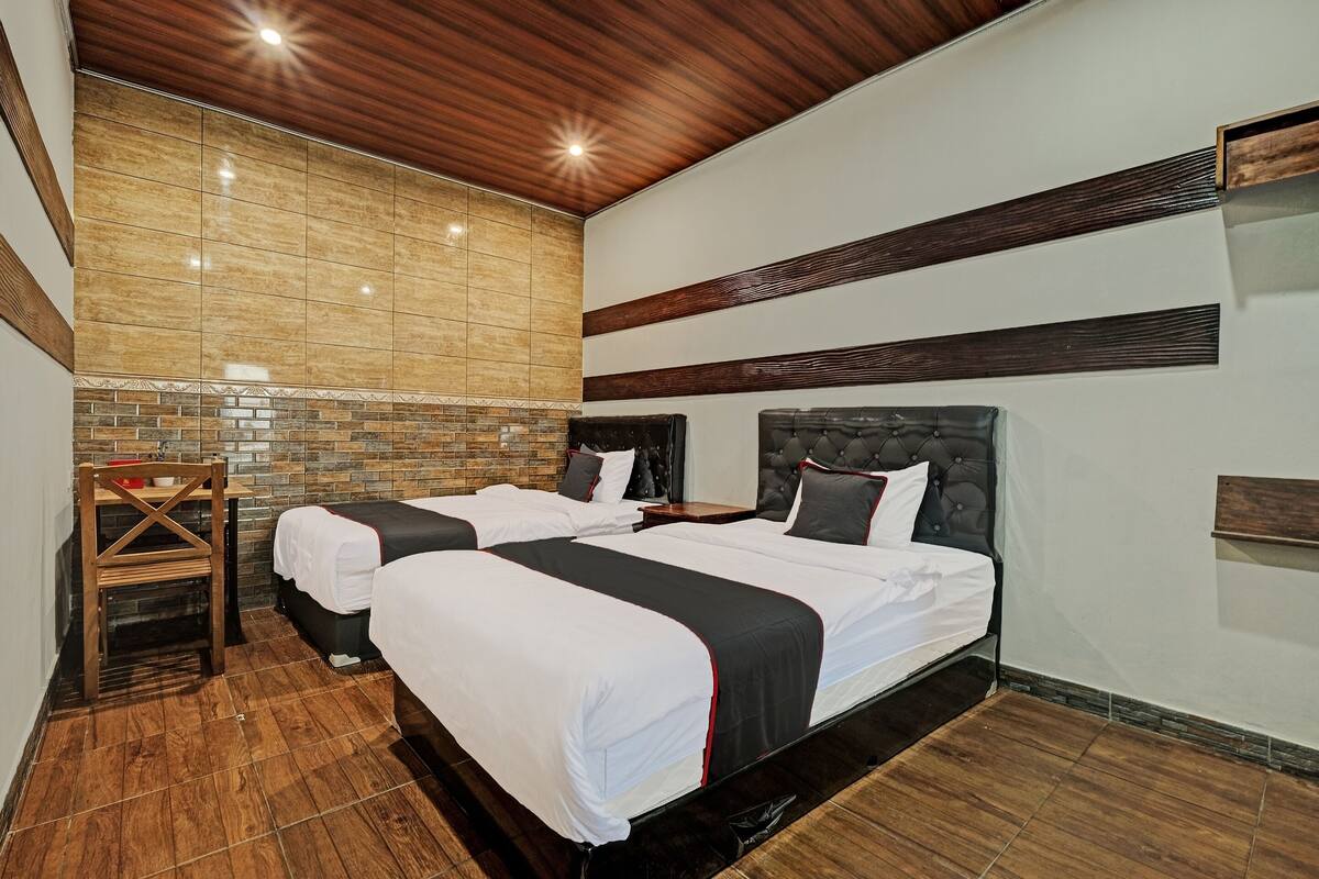 Habitación de hotel con dos camas, techo de madera, pared con azulejos y una pequeña mesa de madera.