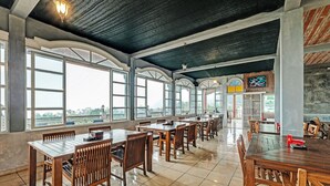 A spacious dining area with wooden tables and chairs, large windows, and a high ceiling. - Capital O 92276 Hotel Pesona Gunung (Getasan)