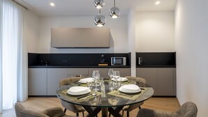 A modern dining area with a glass table, four chairs, and a kitchen in the background.