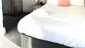 Une chambre d’hôtel avec un grand lit, une table de chevet, une armoire et un tableau représentant un coucher de soleil sur la mer.