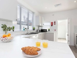 A modern kitchen with white cabinets, a double sink, and a breakfast setup with croissants and orange juice.