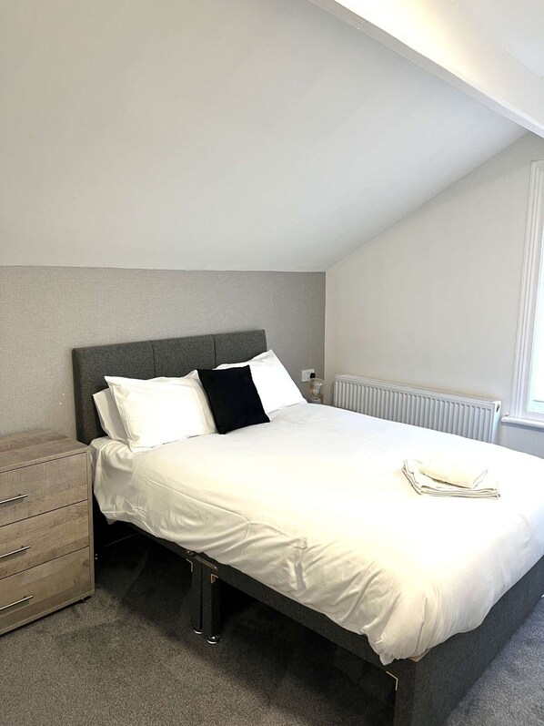 A bedroom with a bed, a nightstand, and a radiator.