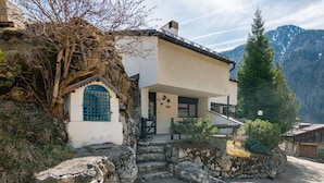 Una casa de campo rústica en la montaña con entrada de piedra, un pequeño porche y vistas de las montañas circundantes.