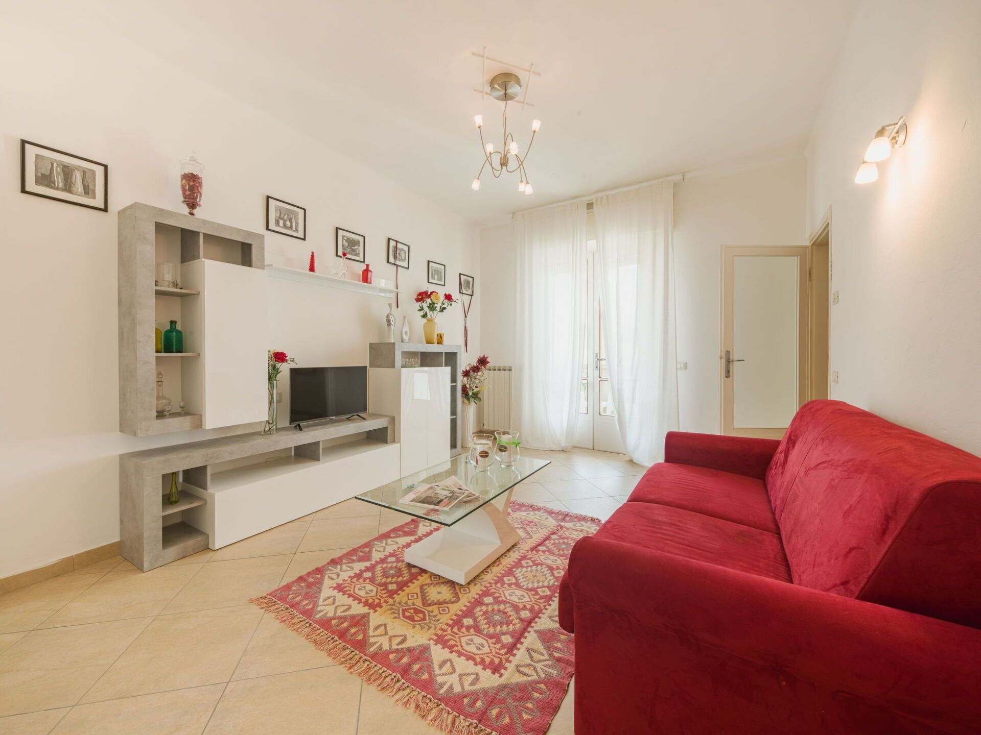 Un soggiorno moderno con un divano rosso, una televisione a schermo piatto, un tavolino da caffè e un tappeto decorato.