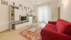 Un salon moderne avec un canapé rouge, un téléviseur à écran plat, une table basse et un tapis à motifs.