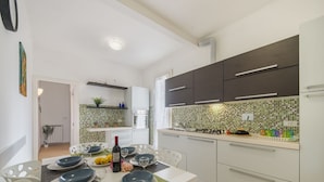 Une cuisine moderne avec des meubles blancs, un pare-feu en carrelage et un coin repas avec une table dressée pour quatre personnes.