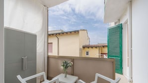 Un balcon avec une table blanche et deux chaises blanches, un petit vase avec des fleurs et une vue sur les immeubles voisins.