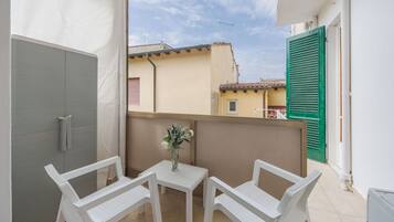 Ein Balkon mit einem weißen Tisch und zwei weißen Stühlen, einer kleinen Vase mit Blumen und Blick auf umliegende Gebäude.